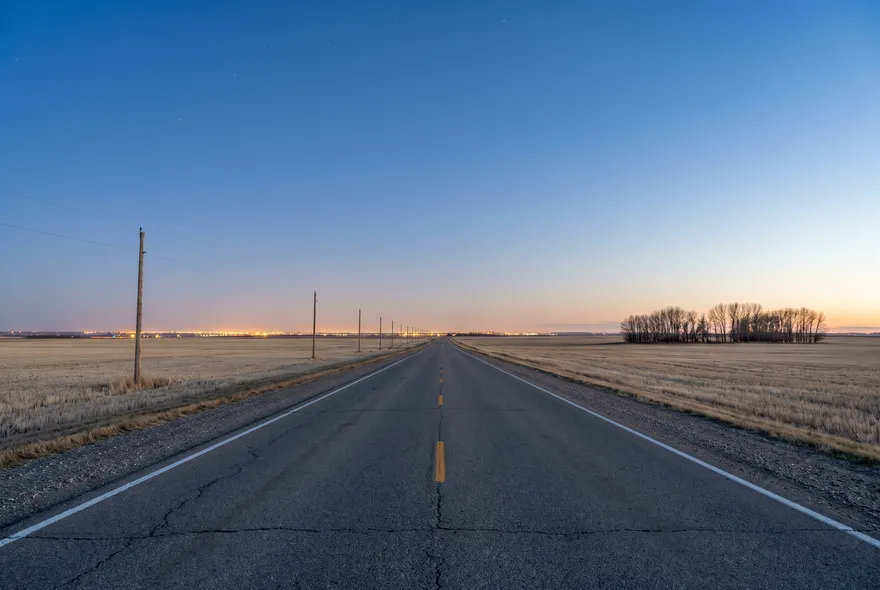 Prairie highway at dusk with city lights ahead